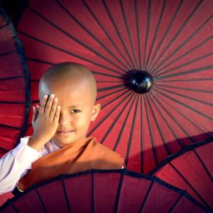 Young Buddhist novice monk smiling with red parasols around