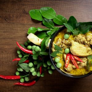 Bowl of Thai green curry chicken with chili peppers and herbs on wooden table