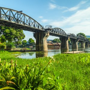 Steel railway bridge over calm river with green vegetation on riverbank