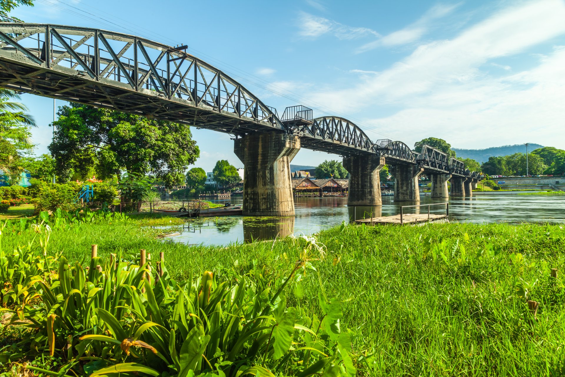 Steel railway bridge over calm river with green vegetation on riverbank
