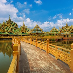 Ornate Thai pavilions with gold and green roofs over water connected by wooden bridge