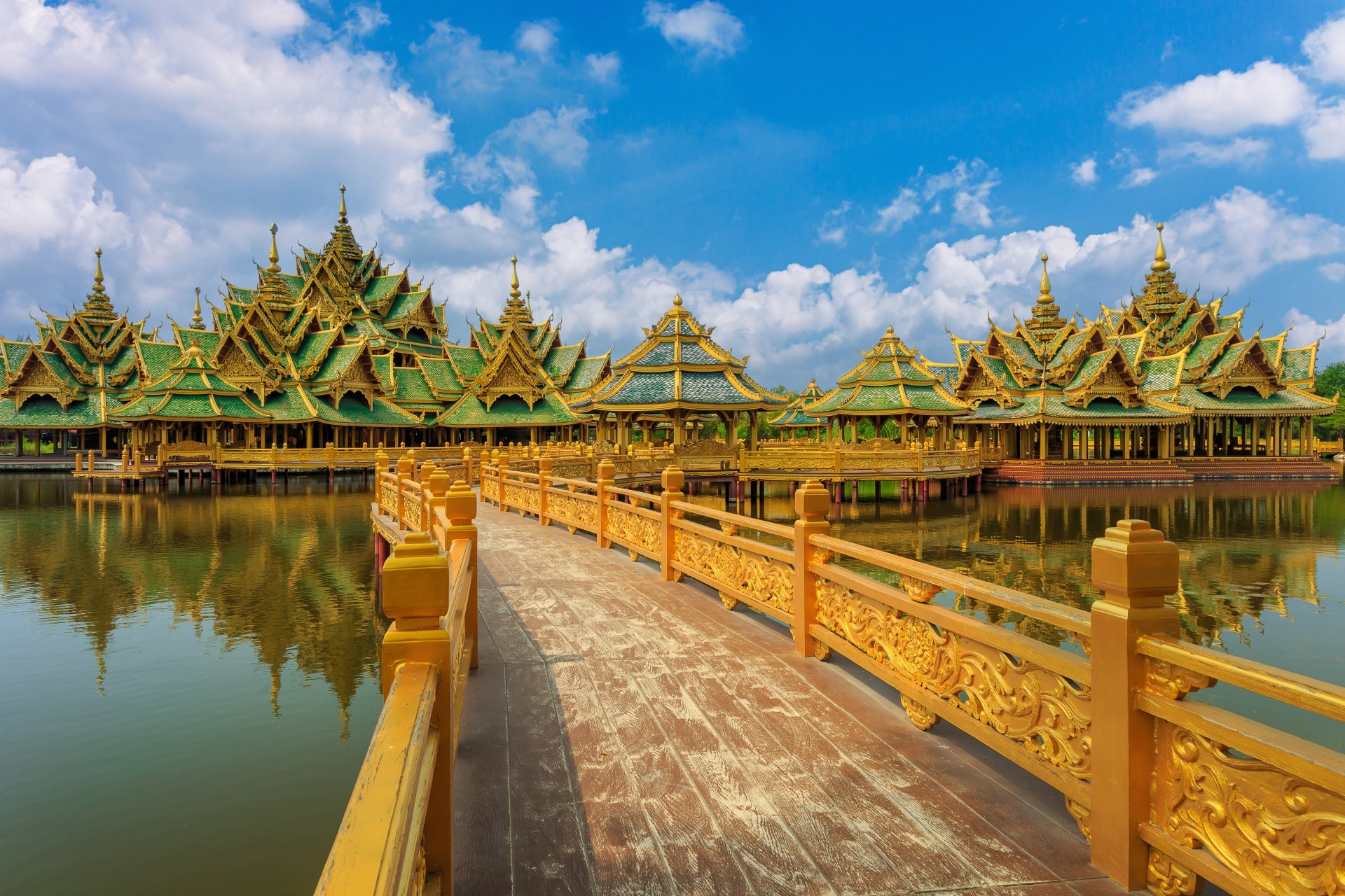 Ornate Thai pavilions with gold and green roofs over water connected by wooden bridge