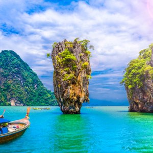 Long-tail boats near tall limestone karst island in turquoise sea under blue sky