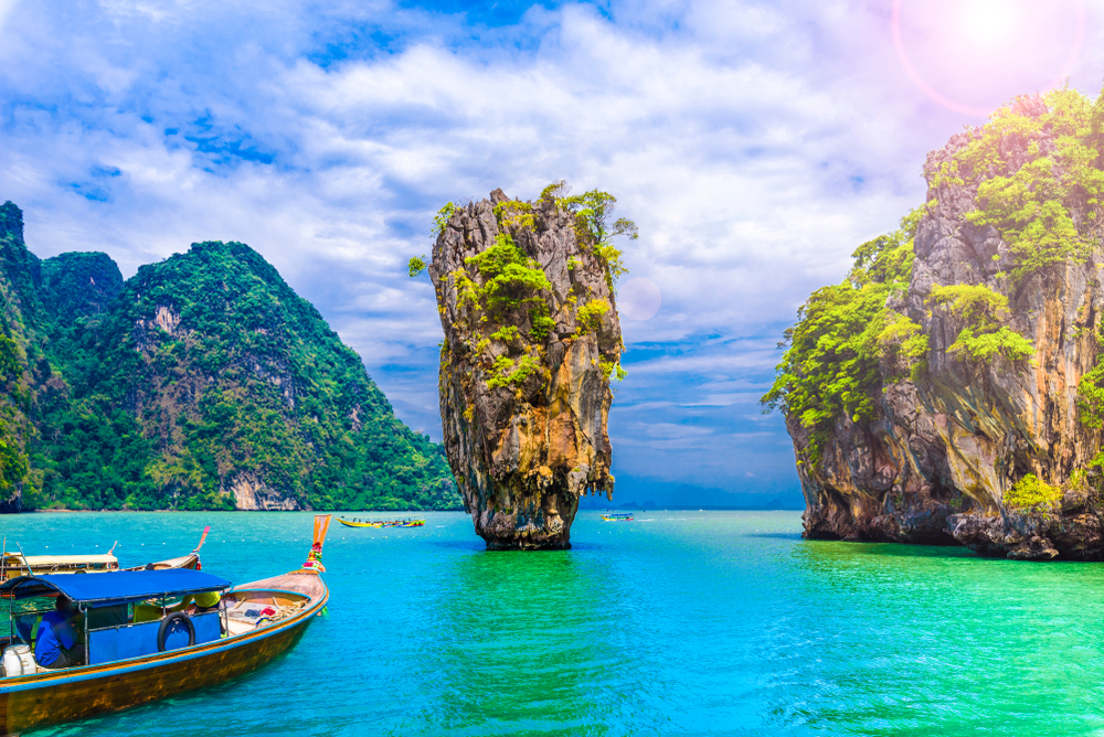 Long-tail boats near tall limestone karst island in turquoise sea under blue sky