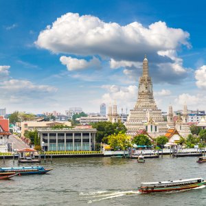 Wat Arun temple by river with boats and cityscape under blue sky