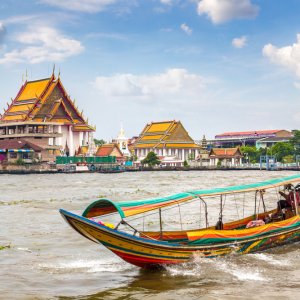 Colorful long-tail boat on river in front of traditional Thai temples with orange roofs