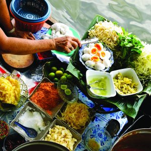 Person preparing traditional Thai food with fresh ingredients by water