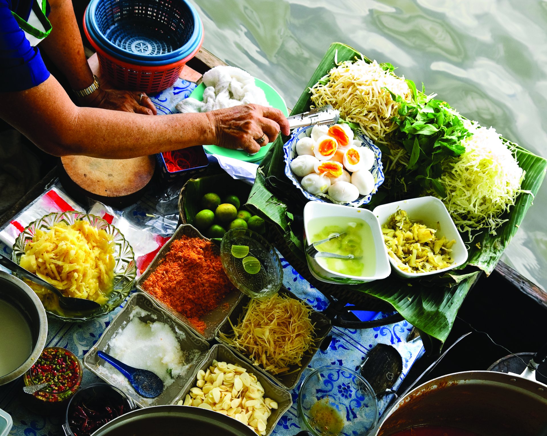 Person preparing traditional Thai food with fresh ingredients by water