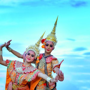 Two traditional Thai dancers in colorful costumes and tall headdresses posing outdoors