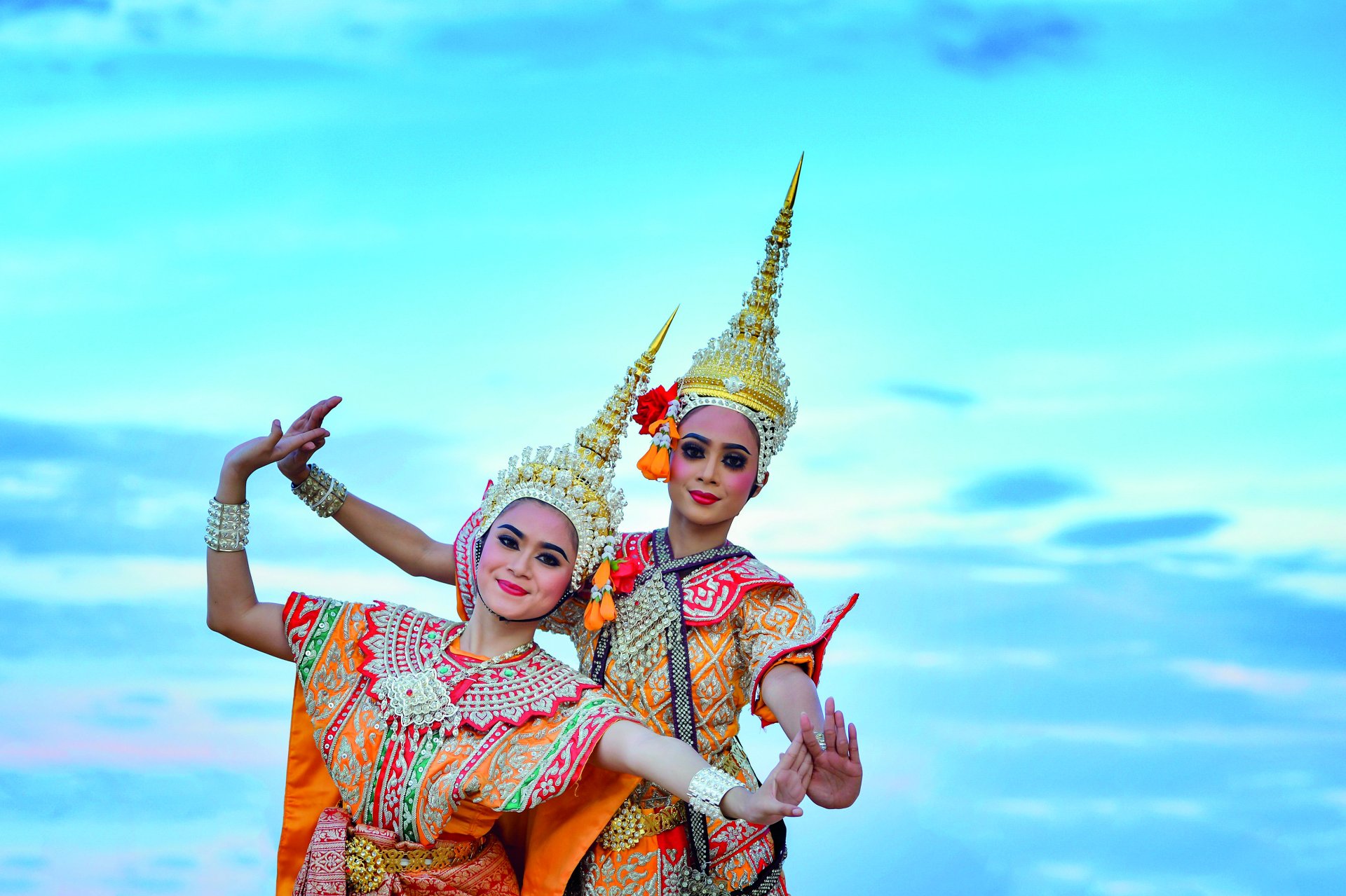 Two traditional Thai dancers in colorful costumes and tall headdresses posing outdoors