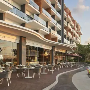 Outdoor dining area with tables and chairs beside Aloft Langkawi Pantai Tengah resort building