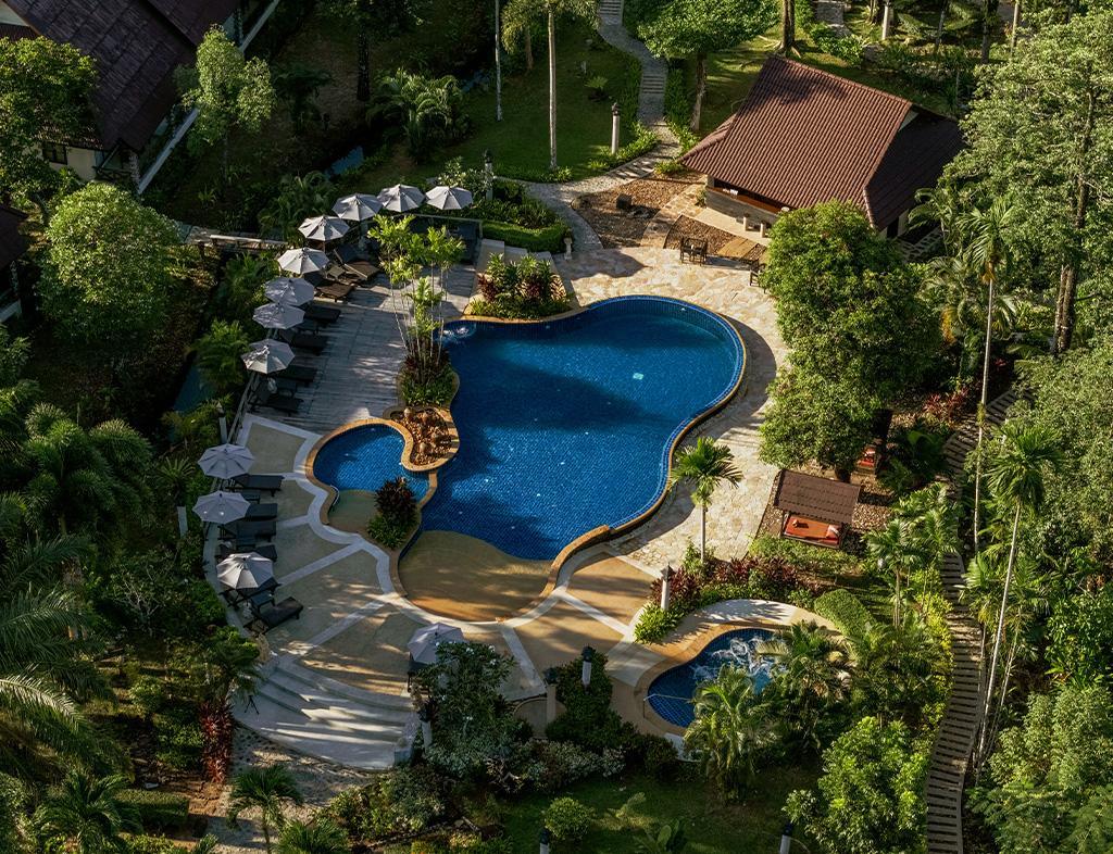 Curved swimming pool with lounge chairs and umbrellas in tropical garden setting