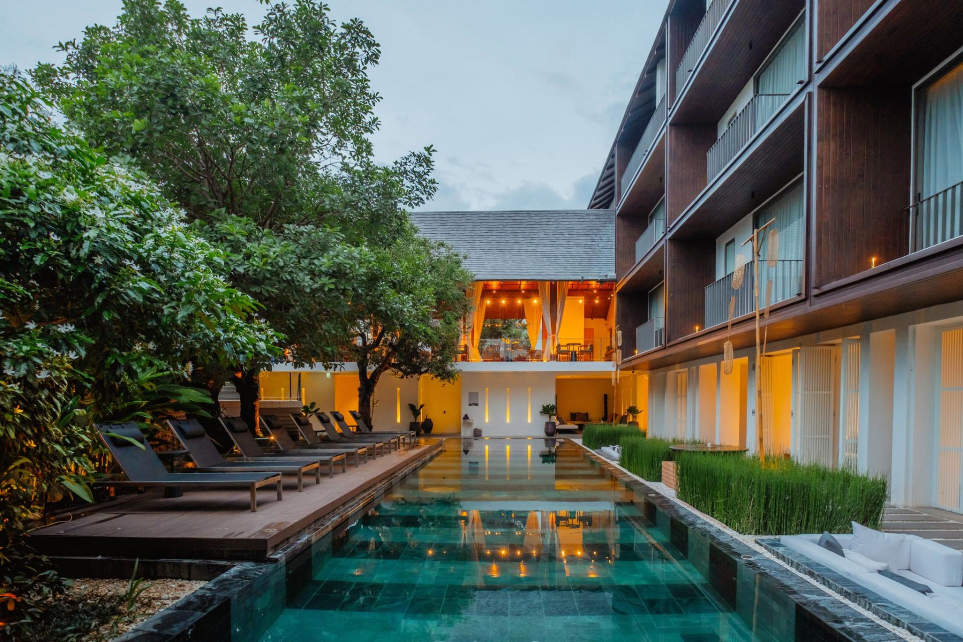 Hotel pool with lounge chairs, plants, and evening lights