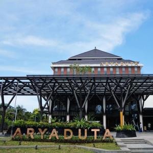 Front entrance of Aryaduta hotel with canopy and large sign surrounded by plants