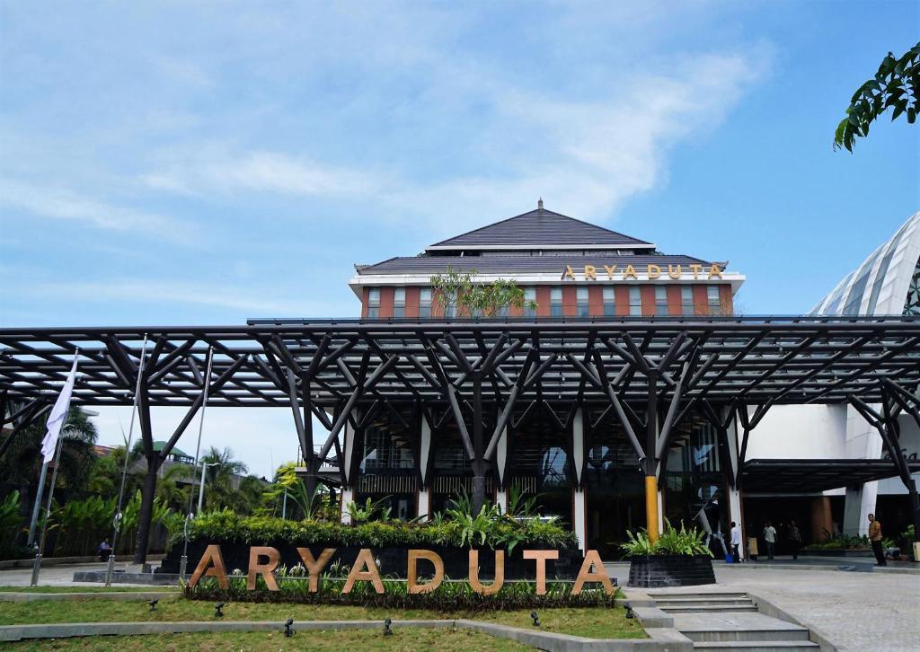 Front entrance of Aryaduta hotel with canopy and large sign surrounded by plants