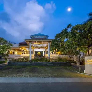 Warmly lit hotel entrance at dusk with tropical plants and palm trees