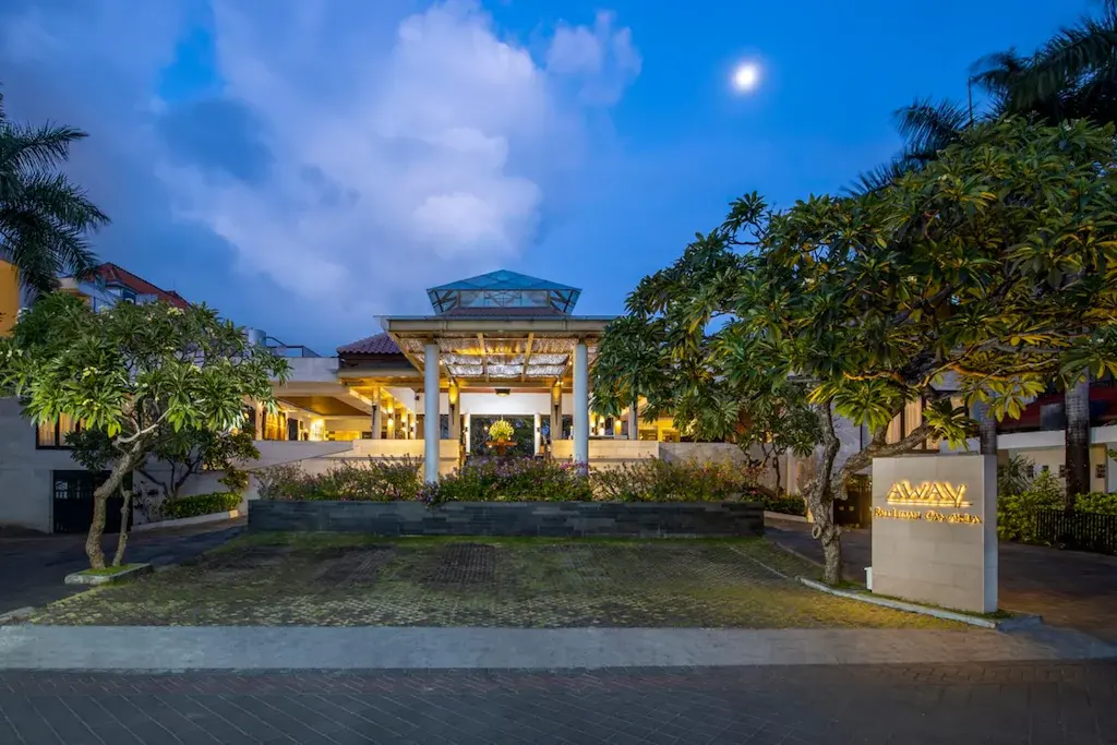 Warmly lit hotel entrance at dusk with tropical plants and palm trees