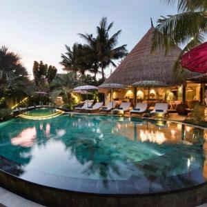 Infinity pool at tropical resort with lounge chairs and thatched roof building at dusk