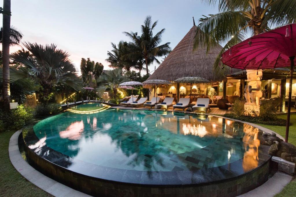 Infinity pool at tropical resort with lounge chairs and thatched roof building at dusk