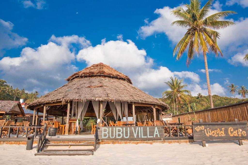 Thatched roof restaurant at BuBu Villa on sandy beach with palm trees and blue sky