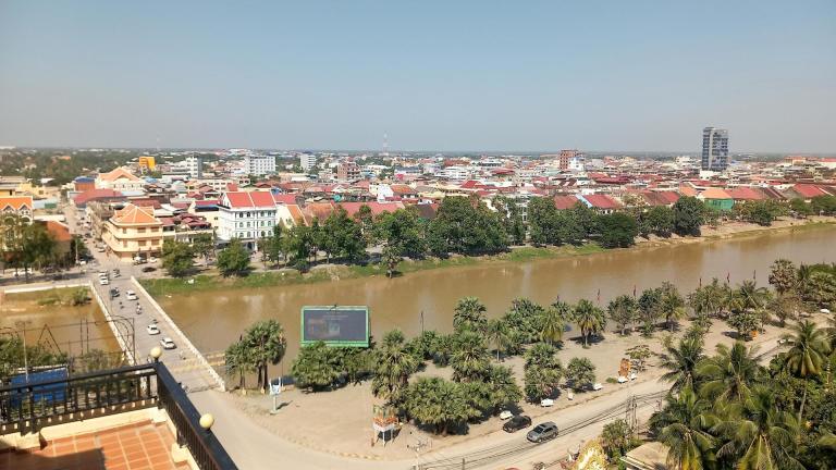 Panoramic view of Battambang city with river, trees, and urban buildings under clear sky