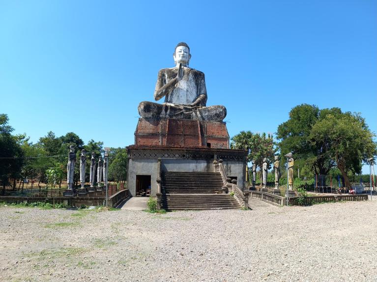 Large seated Buddha statue at temple with standing statues in Battambang Cambodia.