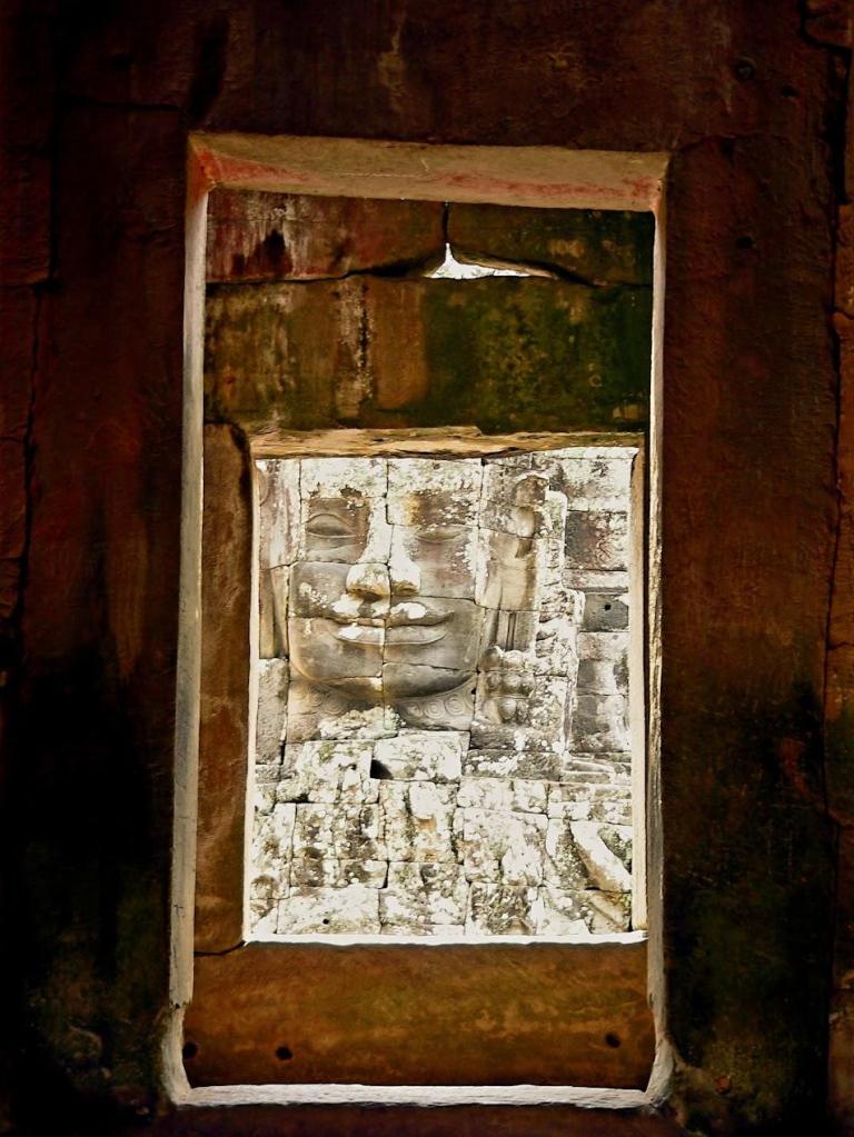 Close-up of an ancient carved stone face seen through a stone window frame inside a temple.