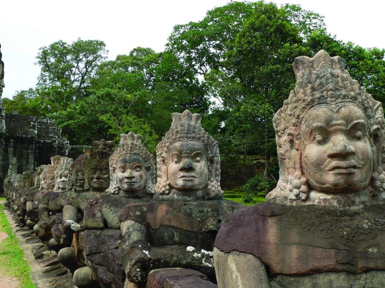 Row of carved ancient stone guardian statues along a path in a green, wooded setting