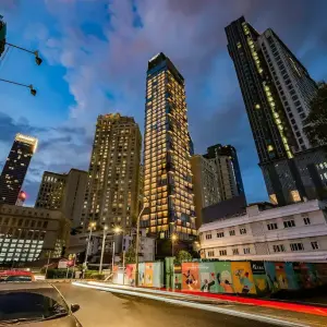 Urban cityscape at dusk featuring illuminated Capri by Fraser Hotel Residences and surrounding buildings.
