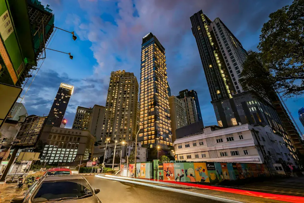 Urban cityscape at dusk featuring illuminated Capri by Fraser Hotel Residences and surrounding buildings.