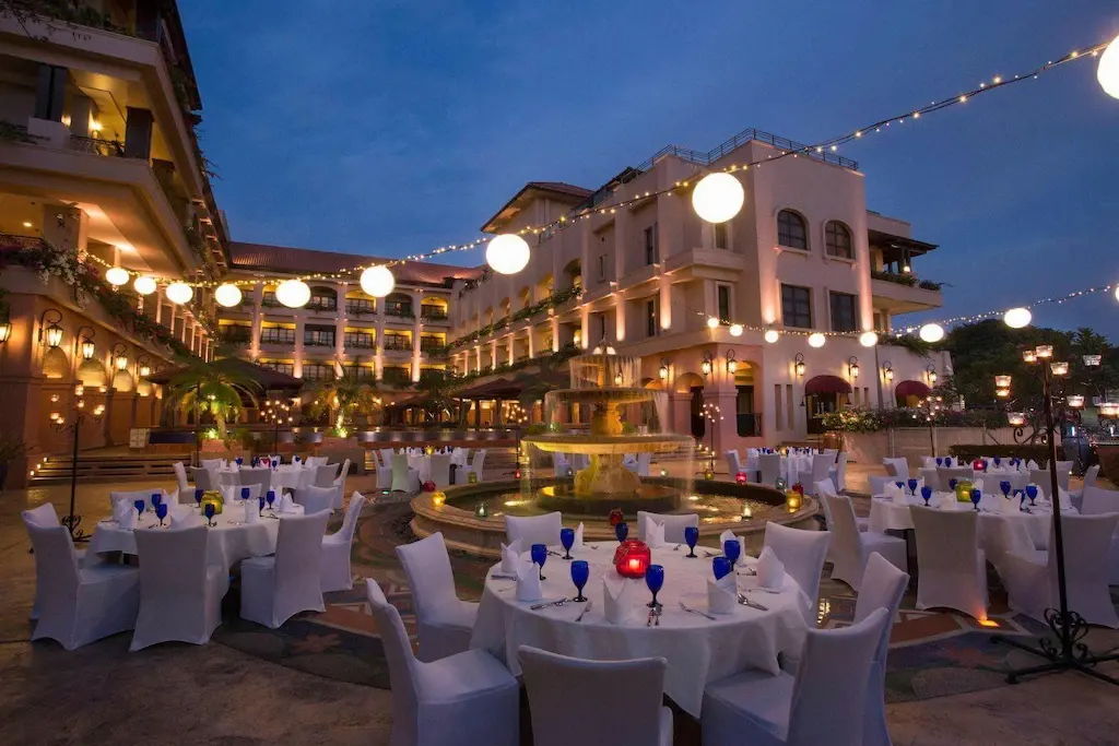 Outdoor dining tables with white covers and blue glasses at Casa del Rio Melaka courtyard at dusk