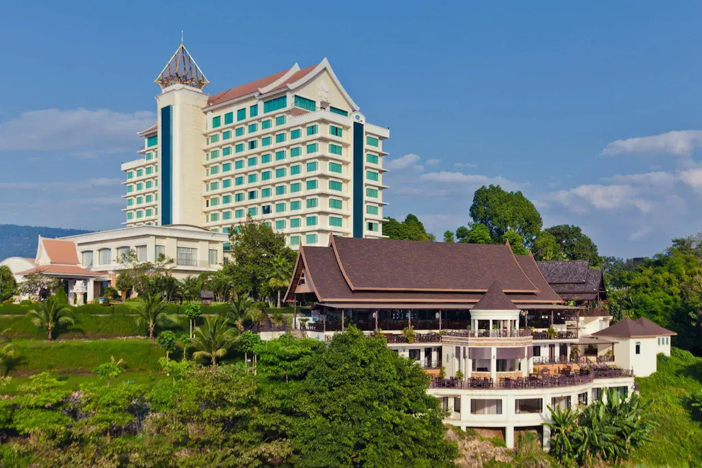 Champasak Grand Hotel building surrounded by green trees and shrubs under blue sky