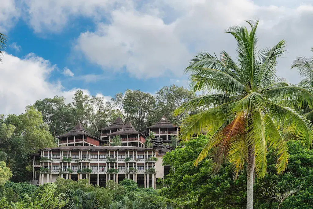 Resort buildings with tiered roofs surrounded by tropical trees and palm under blue sky