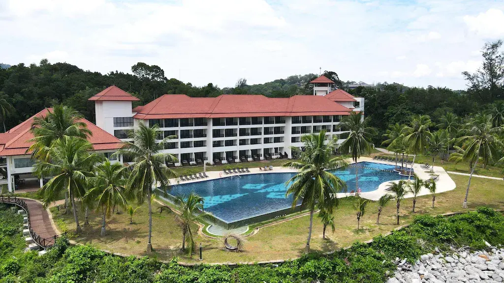 Multi-story resort with red roofs and outdoor pool surrounded by palm trees