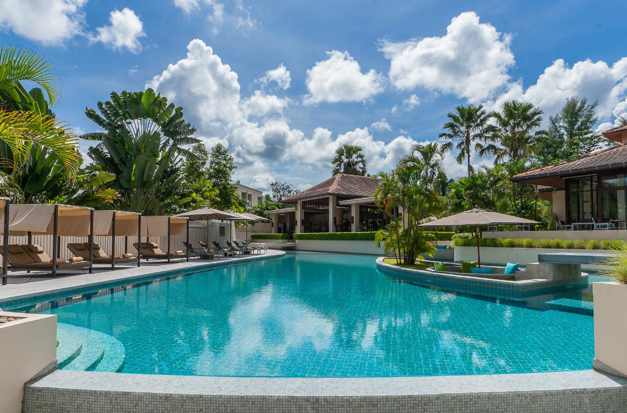 Outdoor resort swimming pool with cabanas, lounge chairs, tropical plants, and a blue sky
