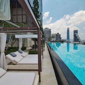 Rooftop infinity pool at EQ Kuala Lumpur with lounge chairs and city skyline under partly cloudy sky.