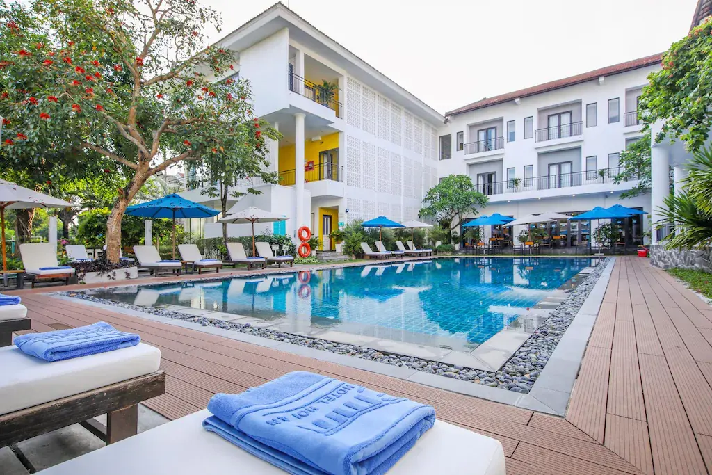 Outdoor swimming pool with sun loungers and umbrellas at Emm Hotel Hoi An