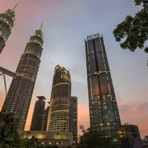 Petronas Twin Towers and Kuala Lumpur skyscrapers at sunset with trees in foreground