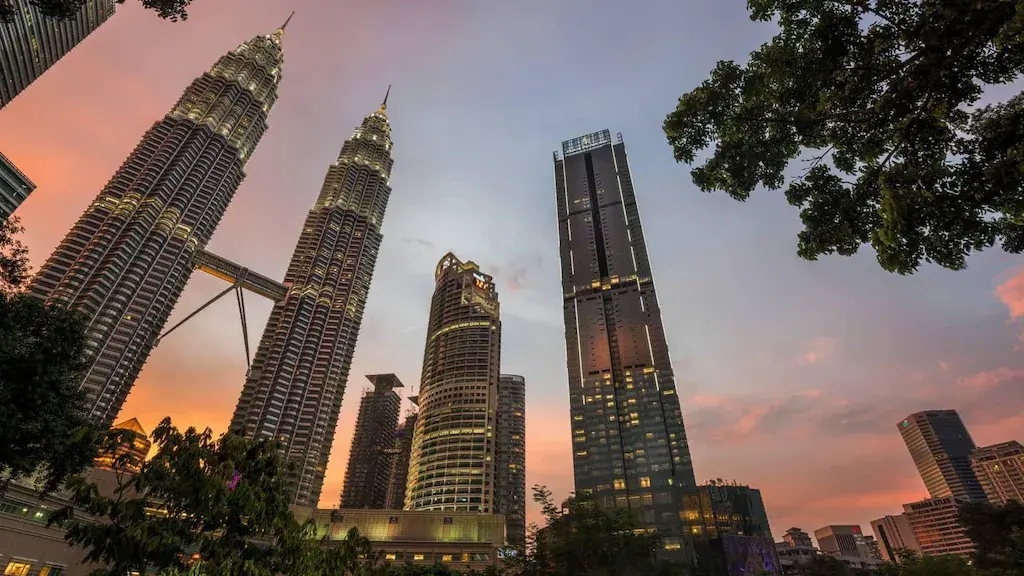 Petronas Twin Towers and Kuala Lumpur skyscrapers at sunset with trees in foreground