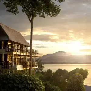 Gaya Island Resort building by water at sunrise with forested hills in background