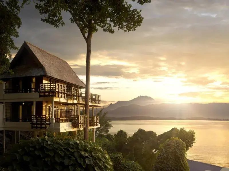 Gaya Island Resort building by water at sunrise with forested hills in background