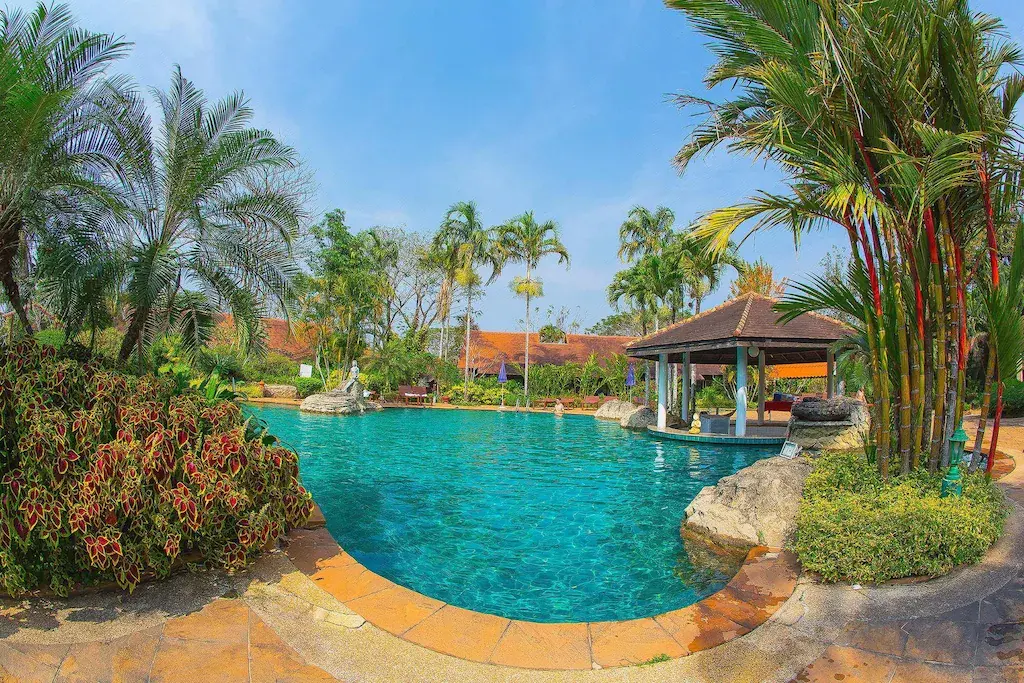 Clear blue swimming pool with palm trees and tropical plants at resort