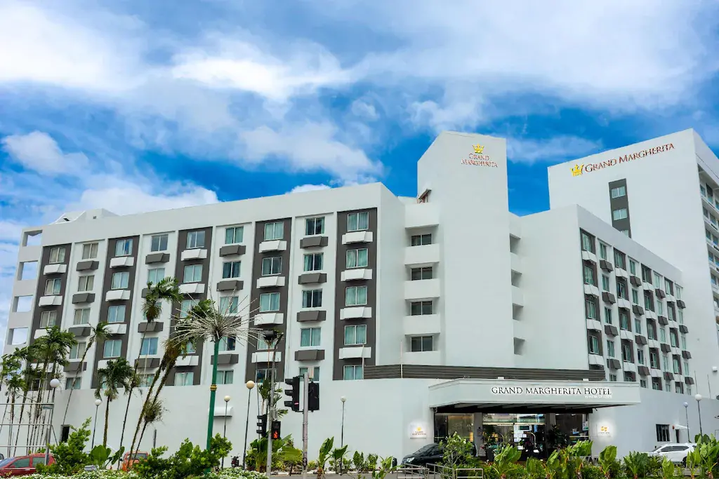 Exterior facade of the Grand Margherita Hotel with palm trees and blue sky