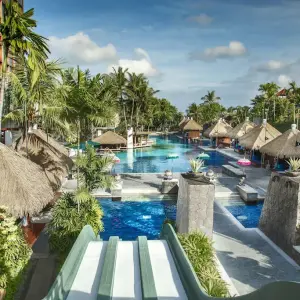 Tropical resort pool with water slides, palm trees, and thatched-roof huts