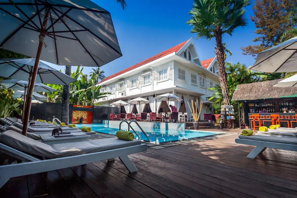 Outdoor pool area with sun loungers, umbrellas, and bar at Homm Maison Souvannaphoum