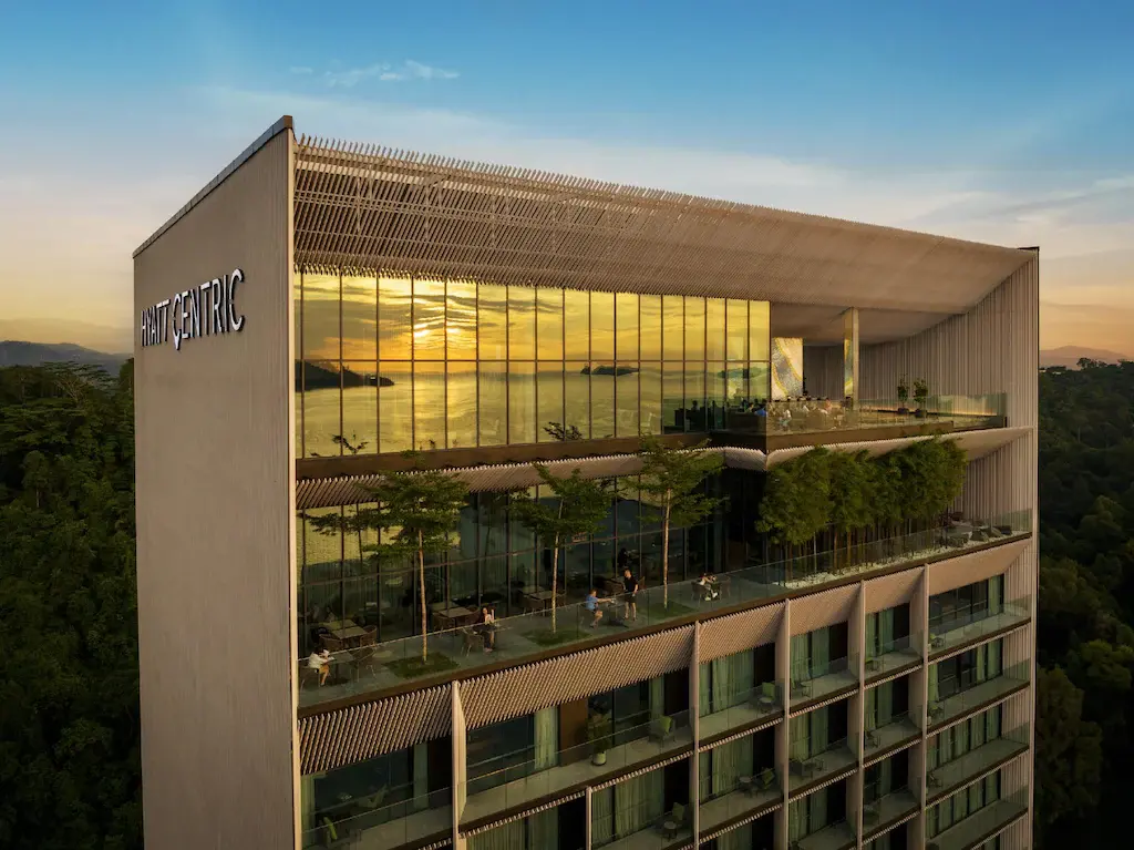 Hyatt Centric Kota Kinabalu hotel exterior with glass windows reflecting sunset and balconies with plants