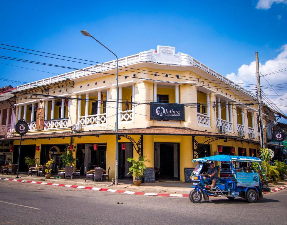 Yellow two-story Inthira Thakhek Hotel with blue tuk-tuk parked outside on street corner