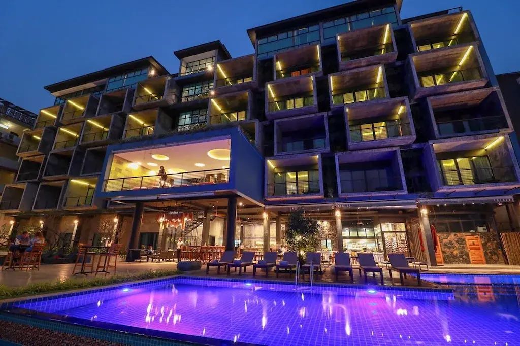 Night exterior of Inthira Vang Vieng hotel with illuminated swimming pool and guests outside