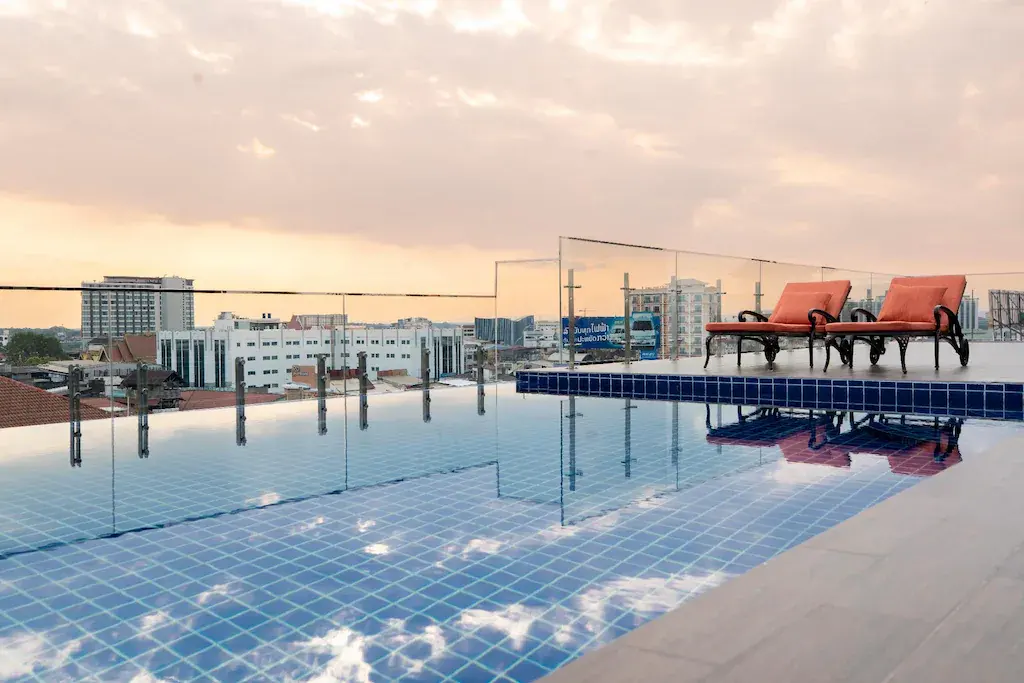 Rooftop pool with two red lounge chairs and city buildings at sunset.