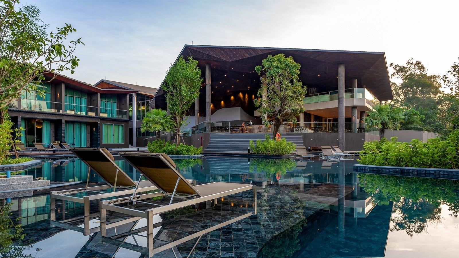 Modern resort pool with lounge chairs and tropical greenery under open-air architecture